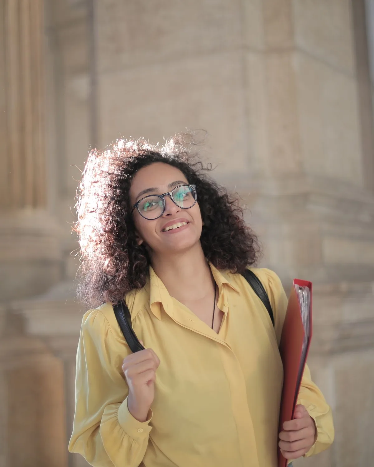 Student with a backpack and folder in front of stone campus columns.